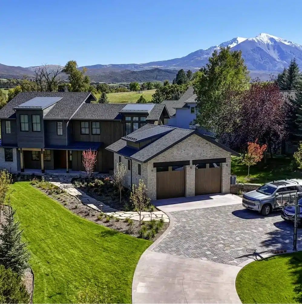 Aerial view of a two-story home with a stone garage, paver driveway and snow-capped Mount Sopris behind