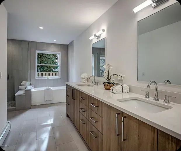 Double vanity with wood cabinets and soaking tub beyond
