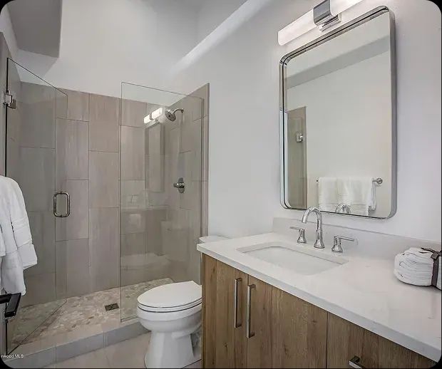 Glass shower beside a wood vanity and tall mirror
