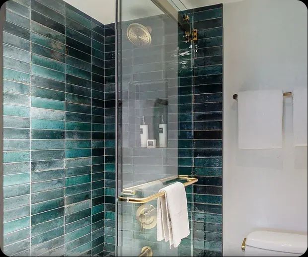 Teal tile shower with brass fixtures and glass door