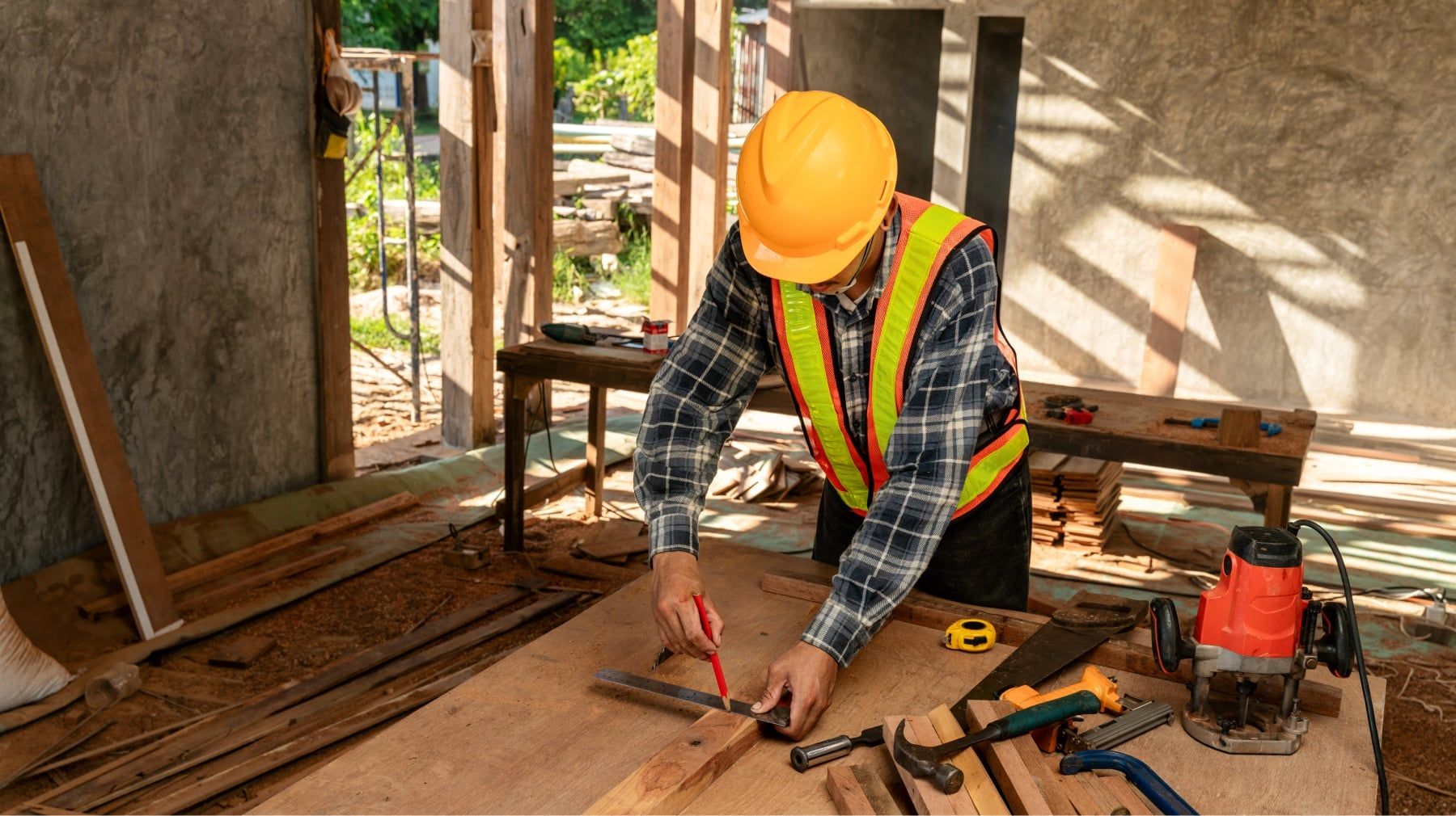 Carpenter in a hard hat and safety vest marking lumber on a workbench at a renovation site