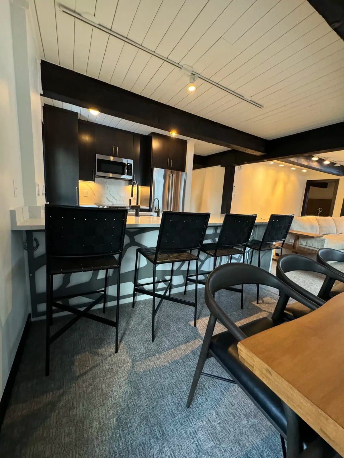 Remodeled condo kitchen with dark cabinets, a marble backsplash and woven bar stools