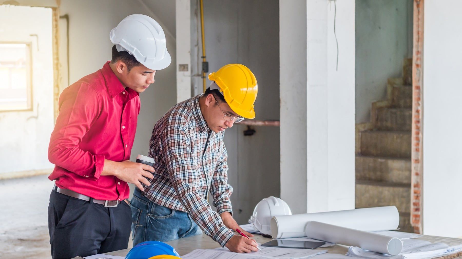 Two contractors in hard hats reviewing plans on site during a home renovation