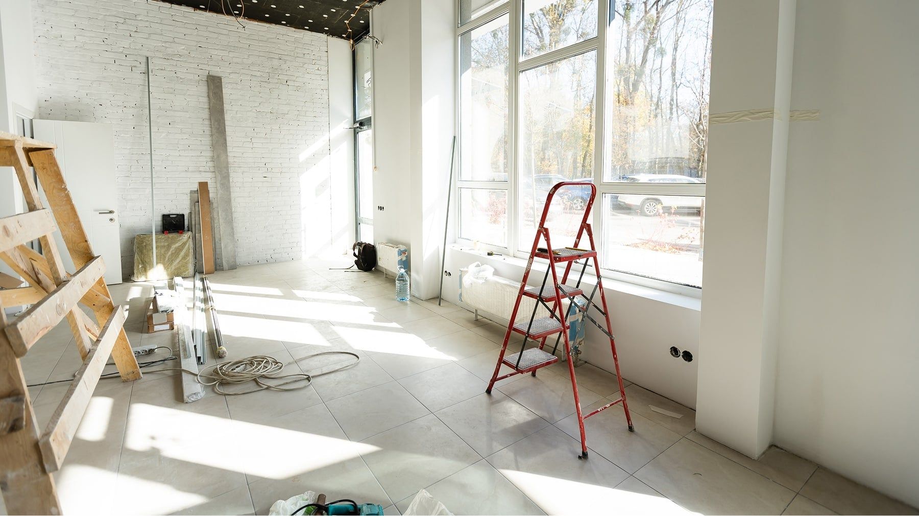 Empty sunlit room under renovation with a red stepladder, sawhorse and tools on a tile floor