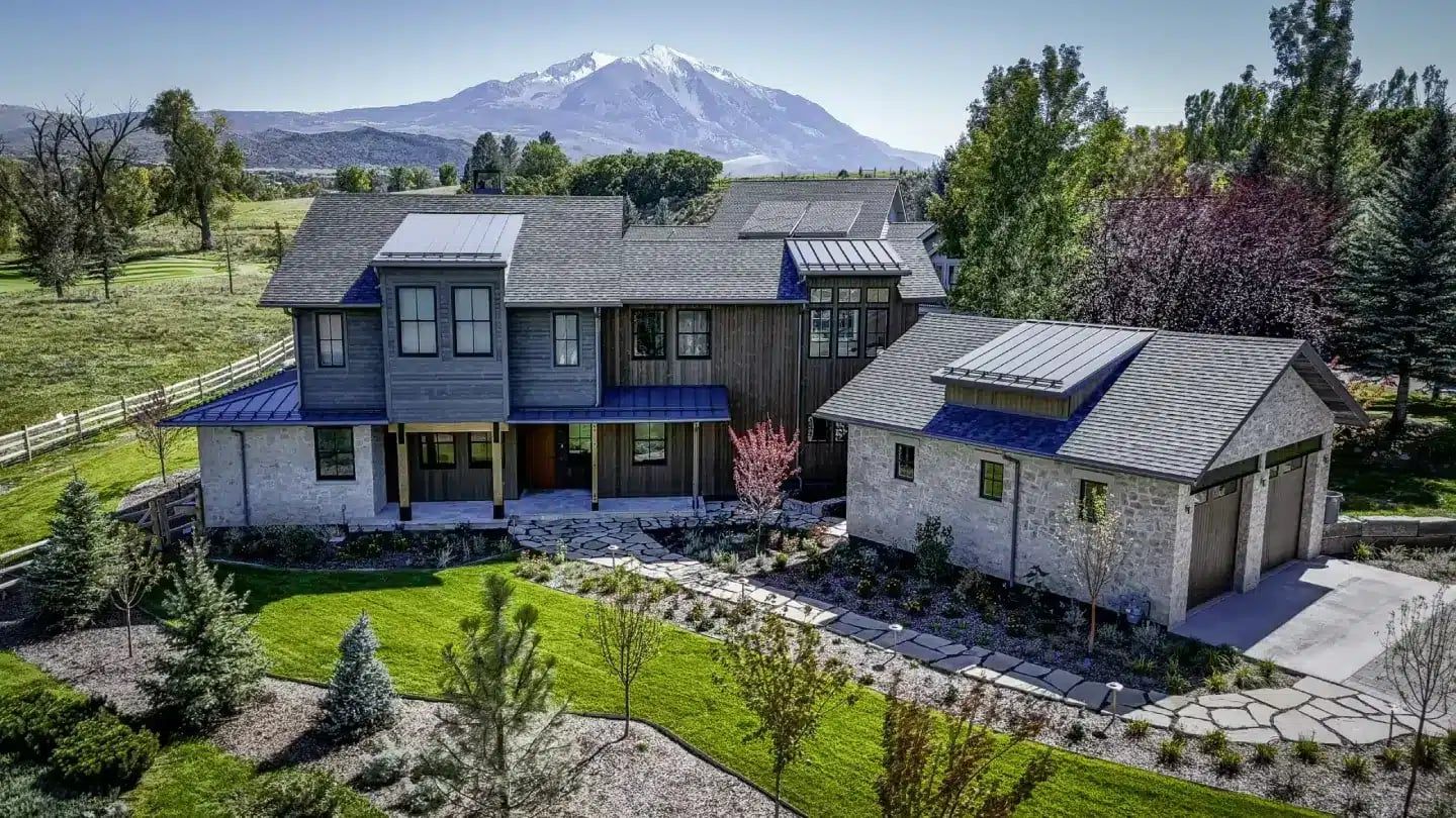Aerial view of a modern farmhouse with stone accents, a metal roof and Mount Sopris in the distance