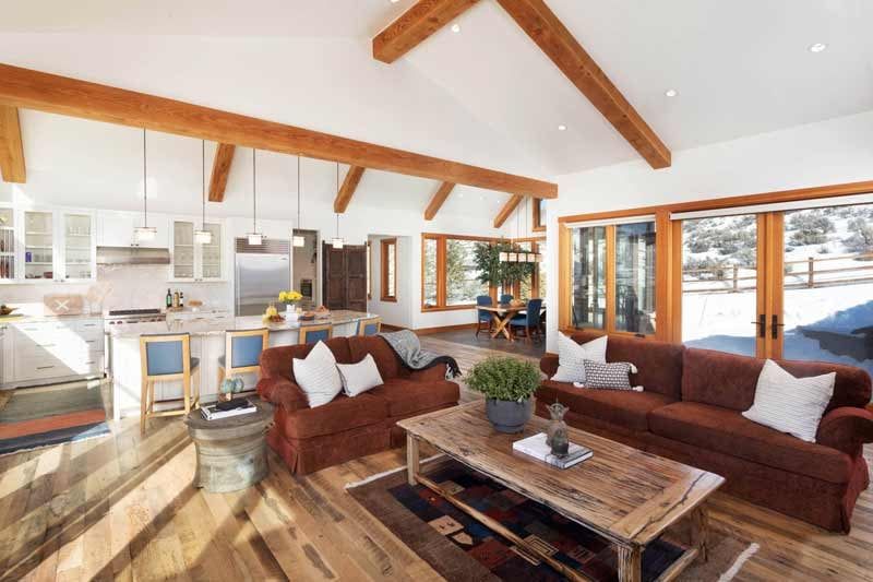 Open great room with exposed wood beams, leather sofas and a white kitchen beyond