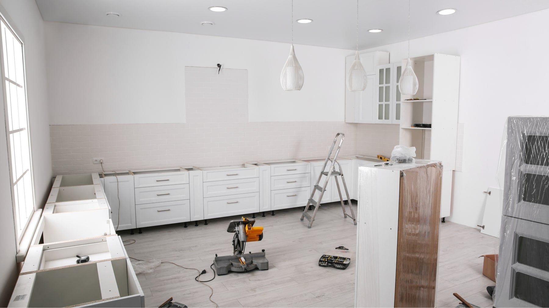 White kitchen cabinets being installed in a bright room with a miter saw on the floor