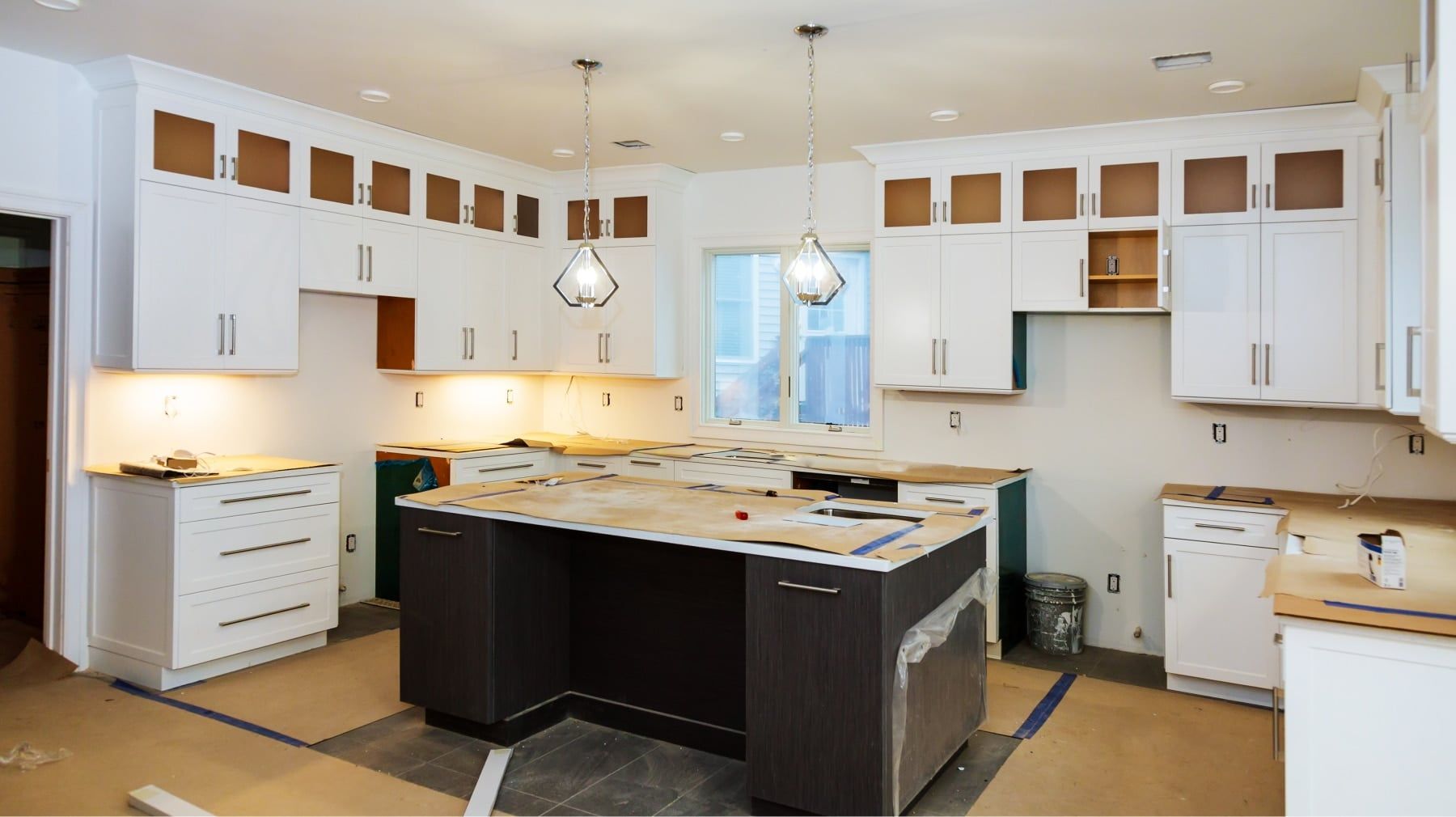 Kitchen remodel in progress with new white cabinets, a dark island and protected countertops