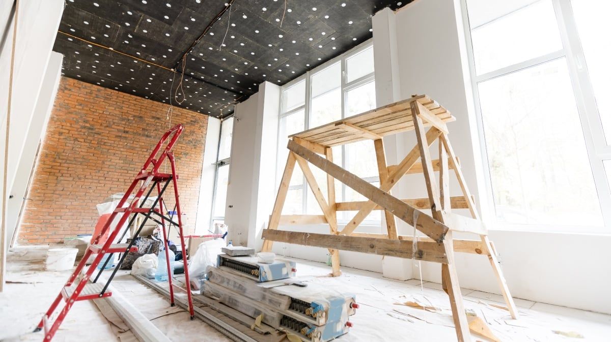 Bright loft interior under renovation with a wooden sawhorse, red ladder and exposed brick wall