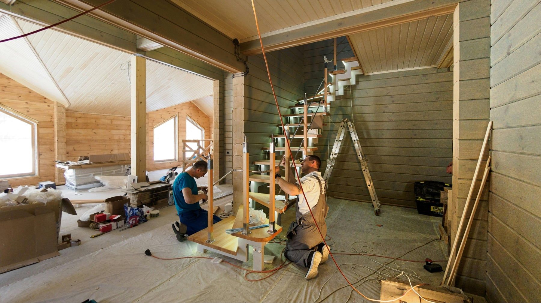 Two carpenters installing a new wooden staircase inside a log home under renovation