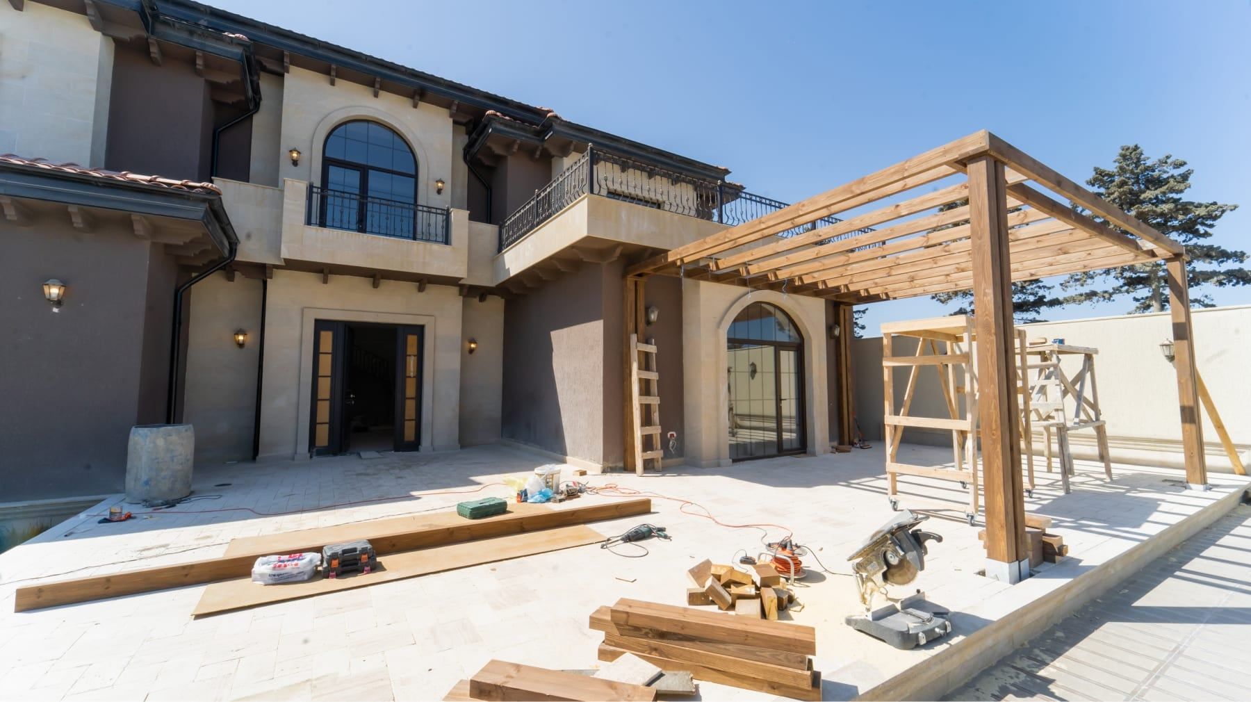 Stucco luxury home exterior with a new timber pergola under construction and lumber on the patio