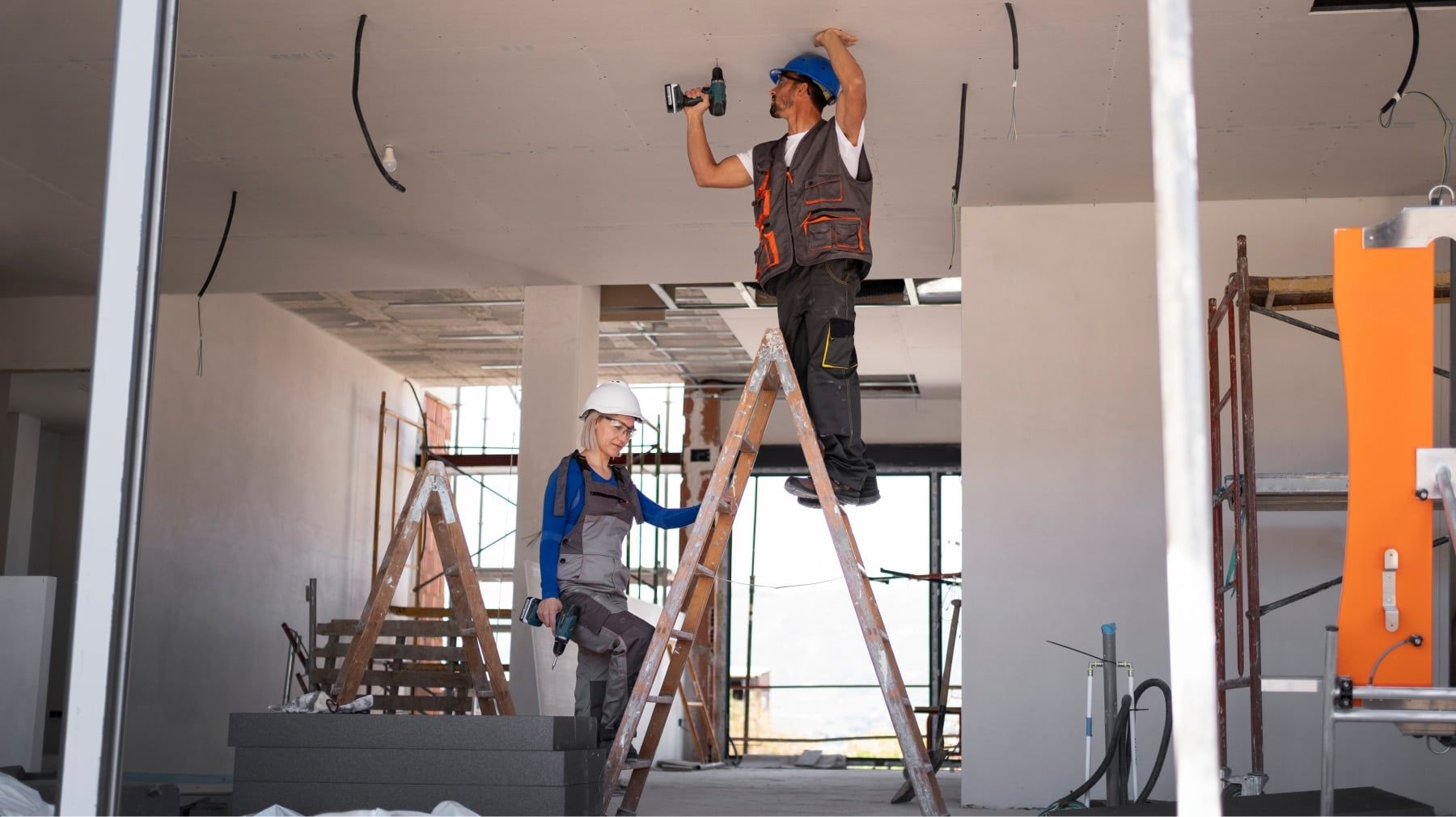 Renovation crew on ladders working on the ceiling of an open interior under construction