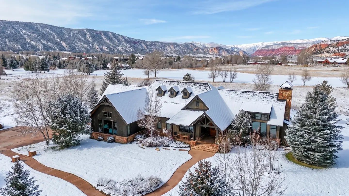 Aerial view of a snowy mountain lodge with a gabled roof and canyon peaks in the distance