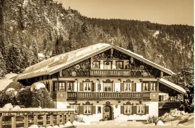 Sepia-toned image of a traditional Alpine chalet with a carved wooden balcony in deep snow