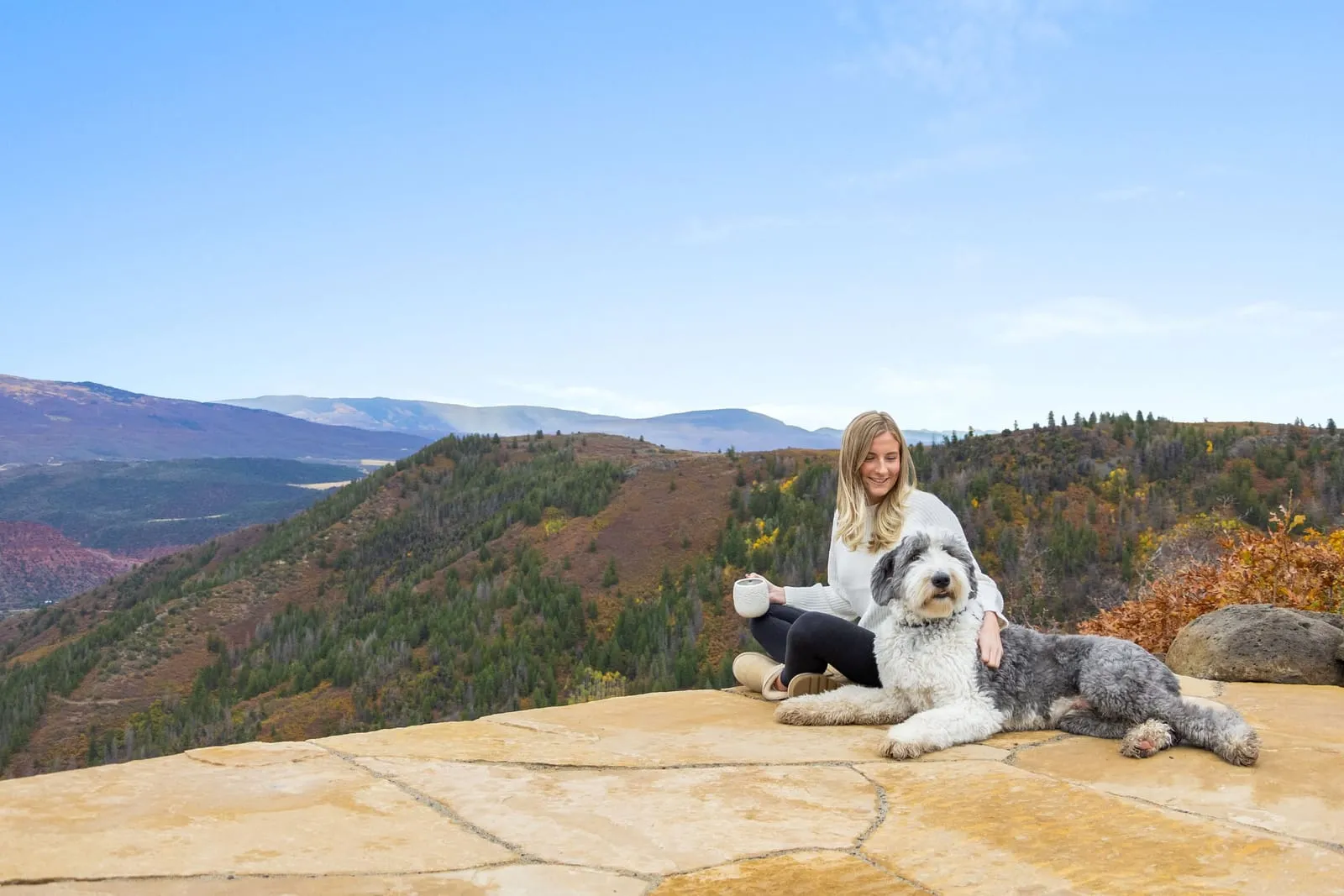 Woman and a sheepdog sitting on the flagstone patio overlooking autumn mountains