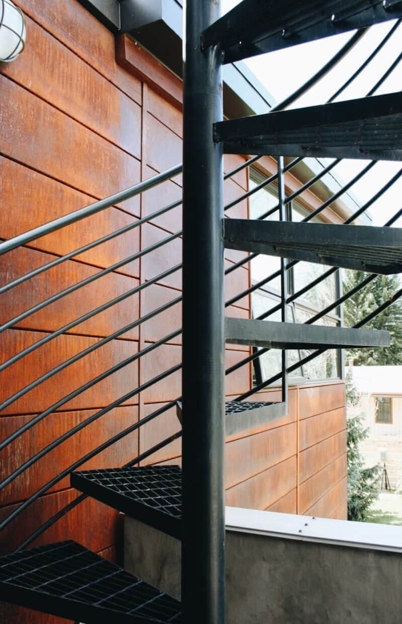 Black steel spiral staircase against weathered steel siding on a mountain home