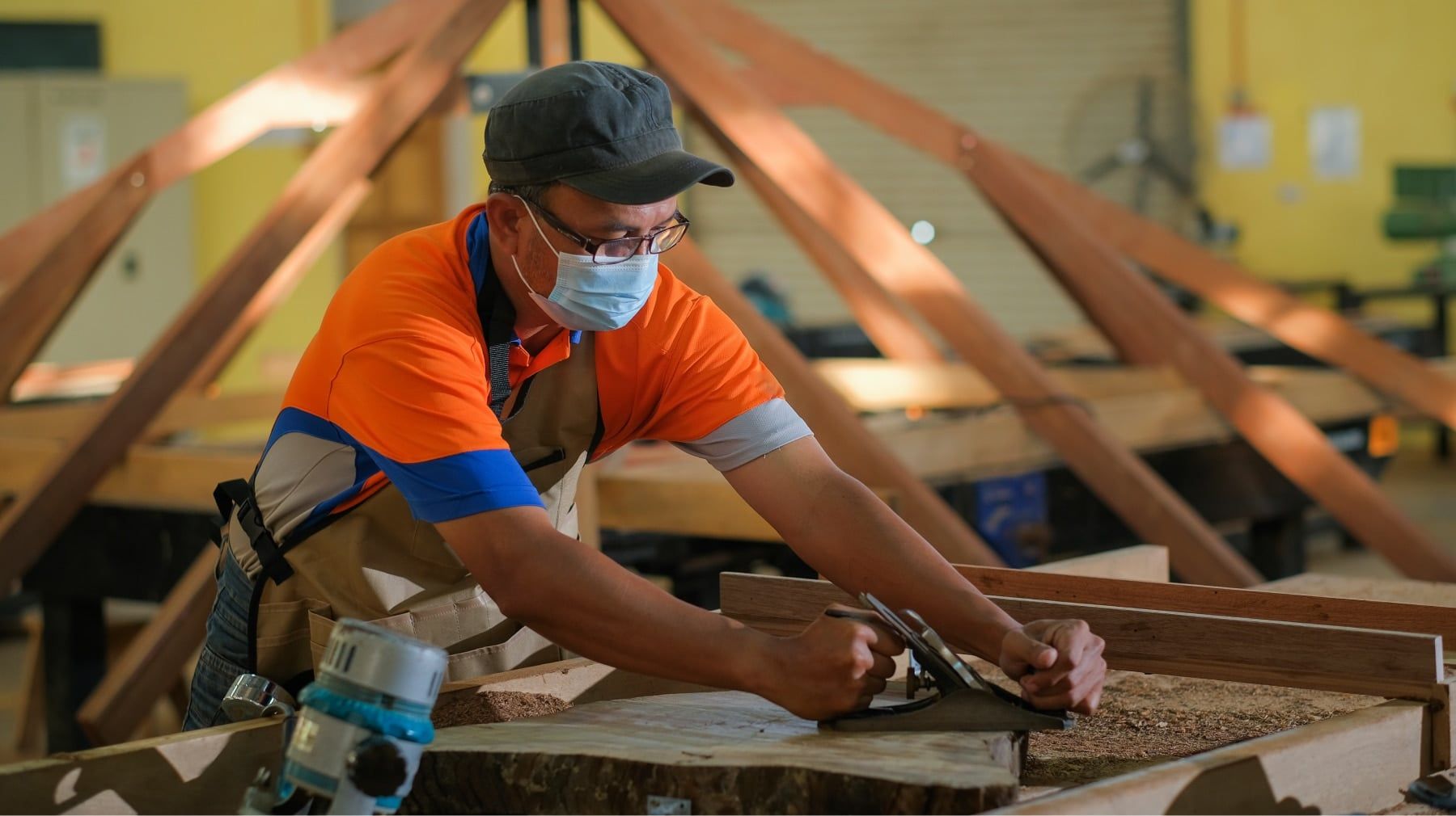 Woodworker in a face mask hand-planing a timber beam in a workshop