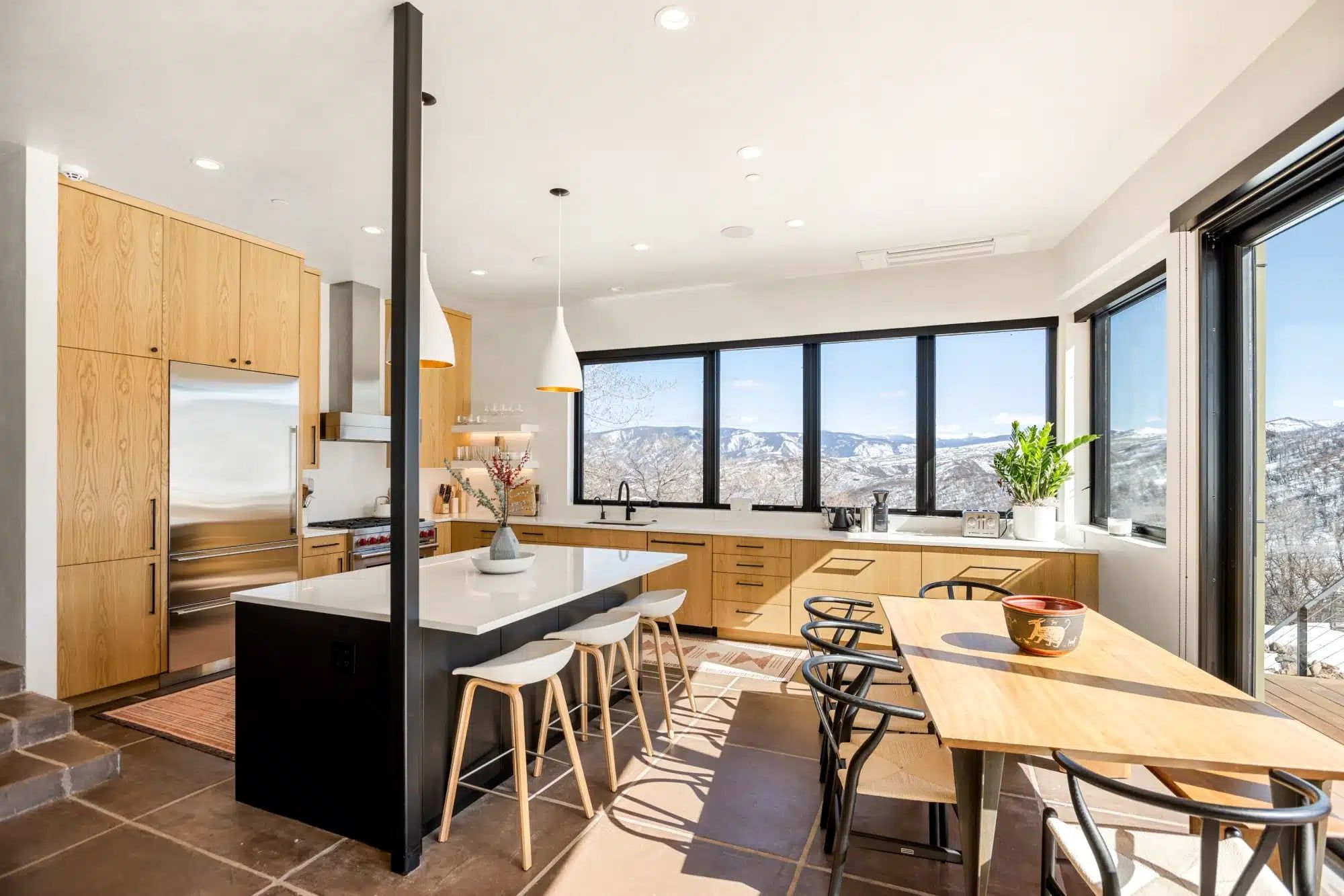 Remodeled mountain kitchen with a black island, bar stools and wide windows facing snowy peaks