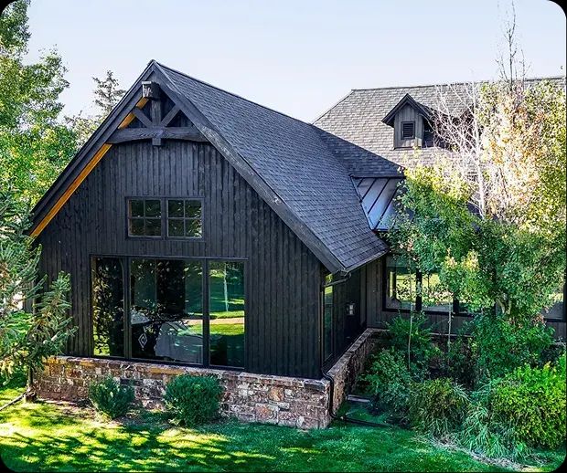 Dark board-and-batten home with stone base and gardens
