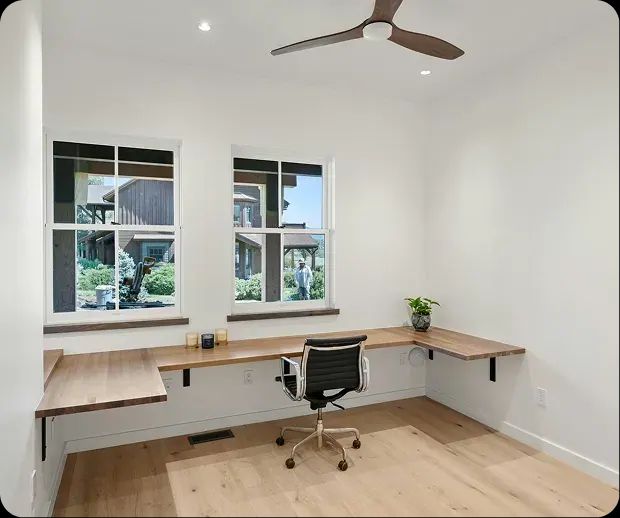 Home office with a floating wood desk under two windows