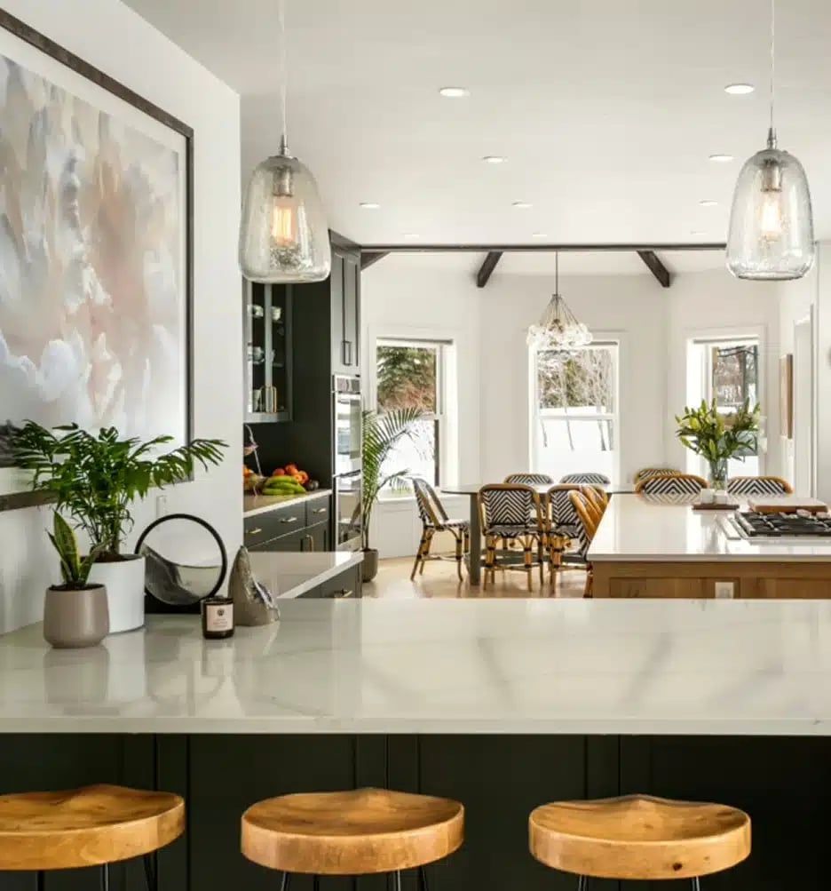 Kitchen with a black island, wood bar stools and glass pendants opening to a bright dining area
