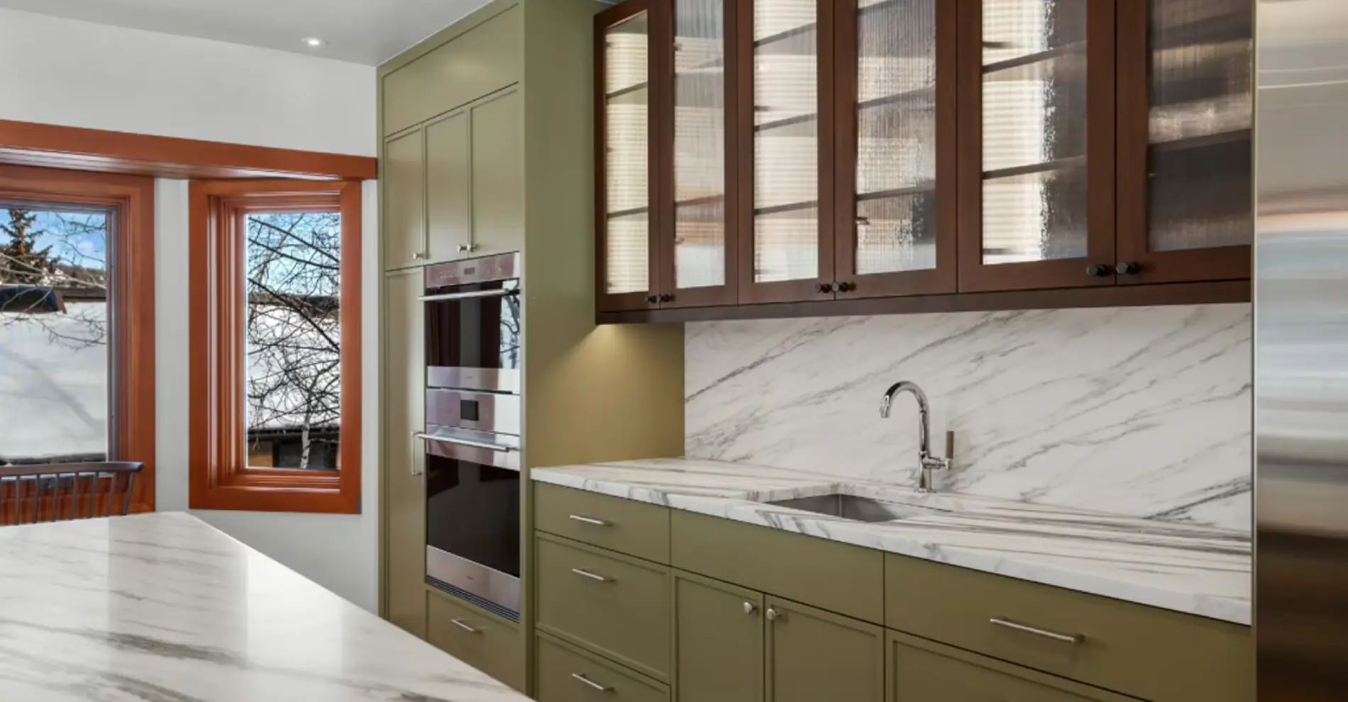 Kitchen with olive green cabinets, glass-front upper cabinets and a marble backsplash