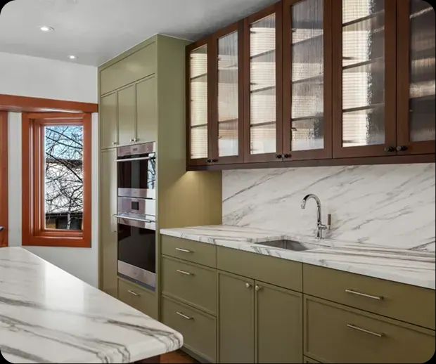 Olive green cabinets with glass-front uppers and marble counters