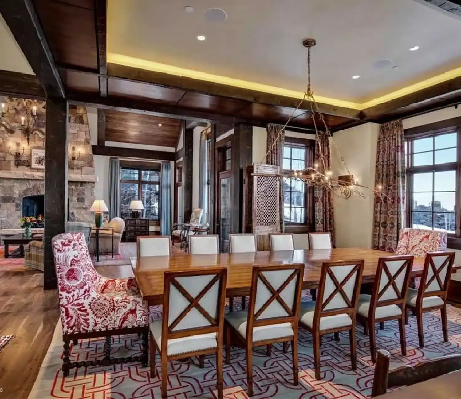 Mountain home dining room with timber beams, a branch chandelier and a stone fireplace beyond