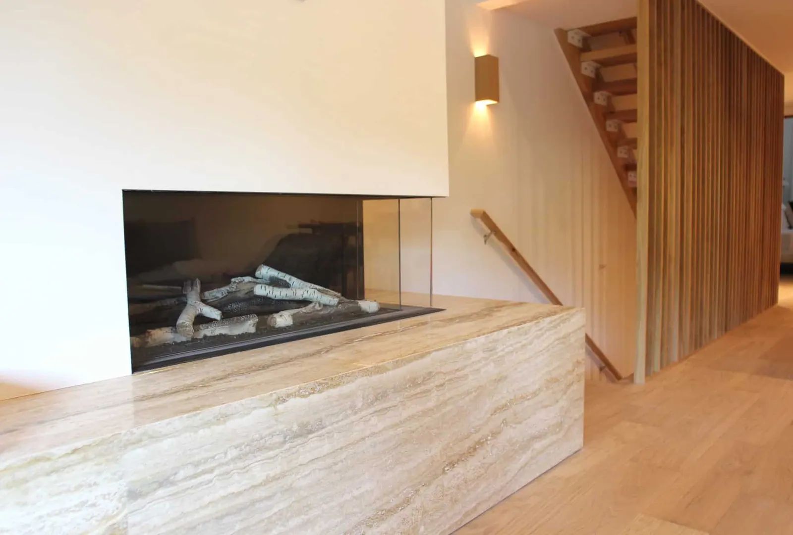 Linear gas fireplace with a travertine hearth beside a wood-clad staircase