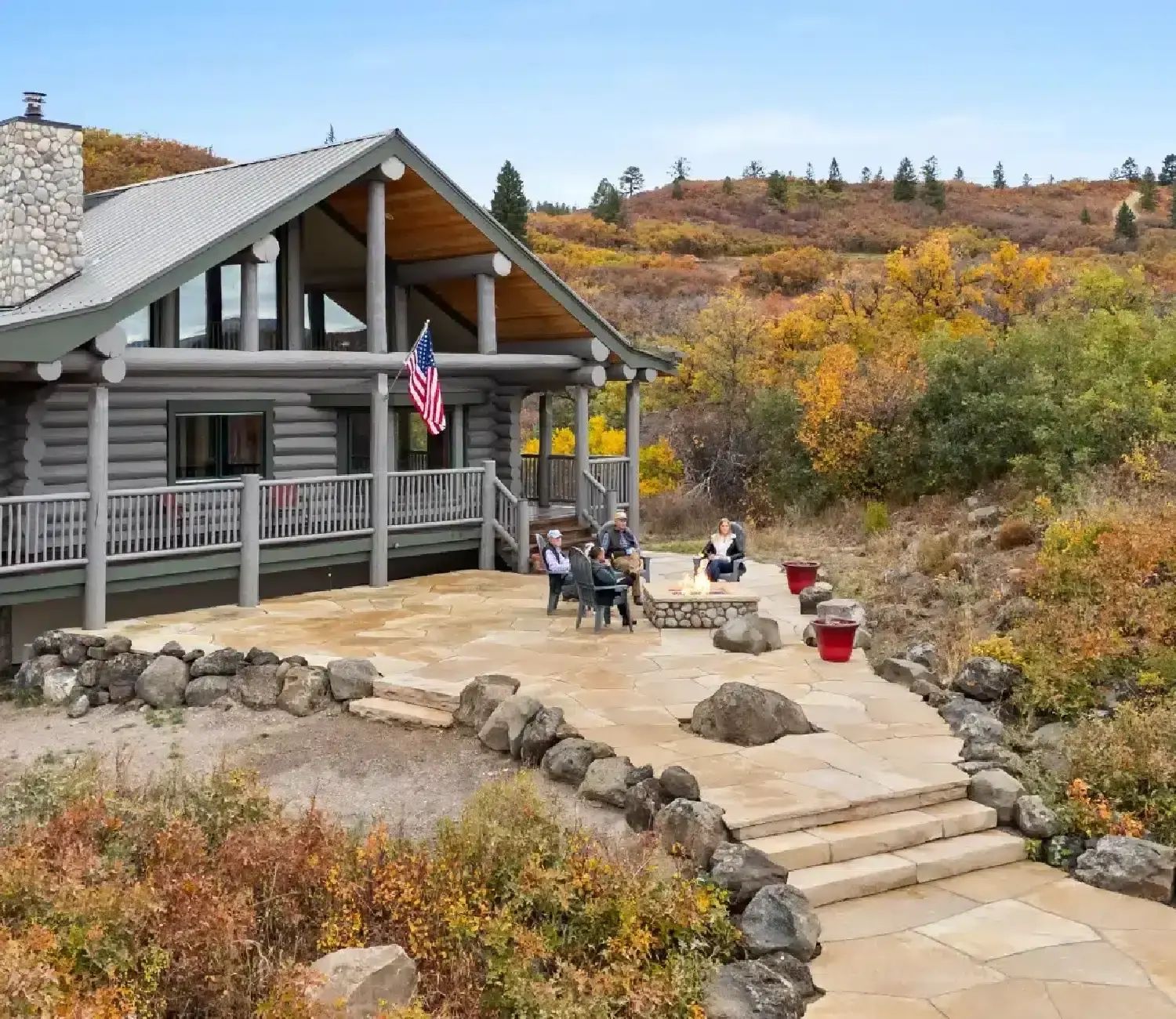 Log home with a stone patio and steps among autumn shrubs