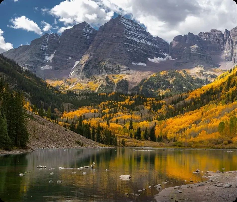 Maroon Bells reflected in a lake surrounded by golden autumn aspens