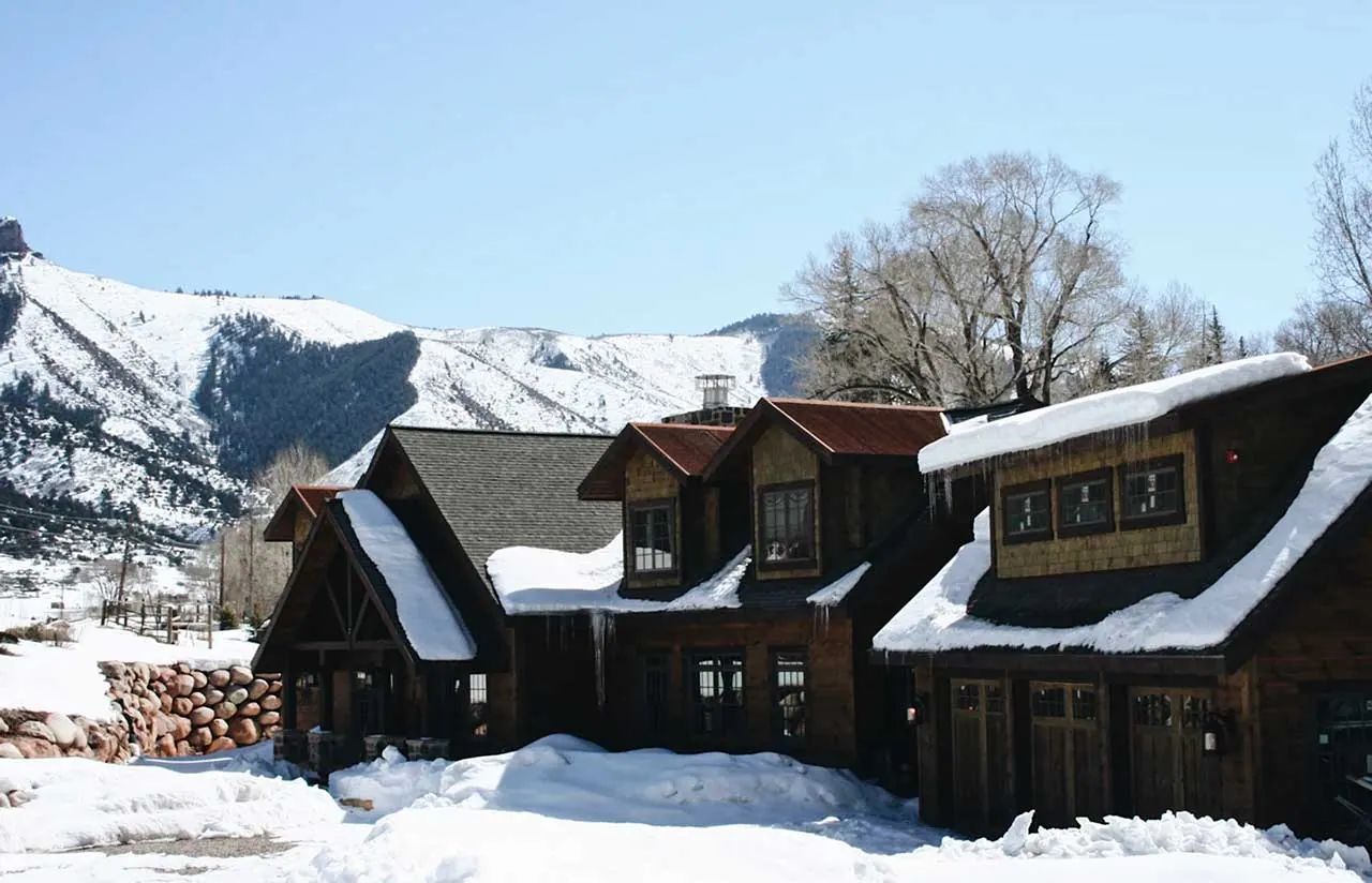 Dark timber mountain home covered in winter snow below a ski slope