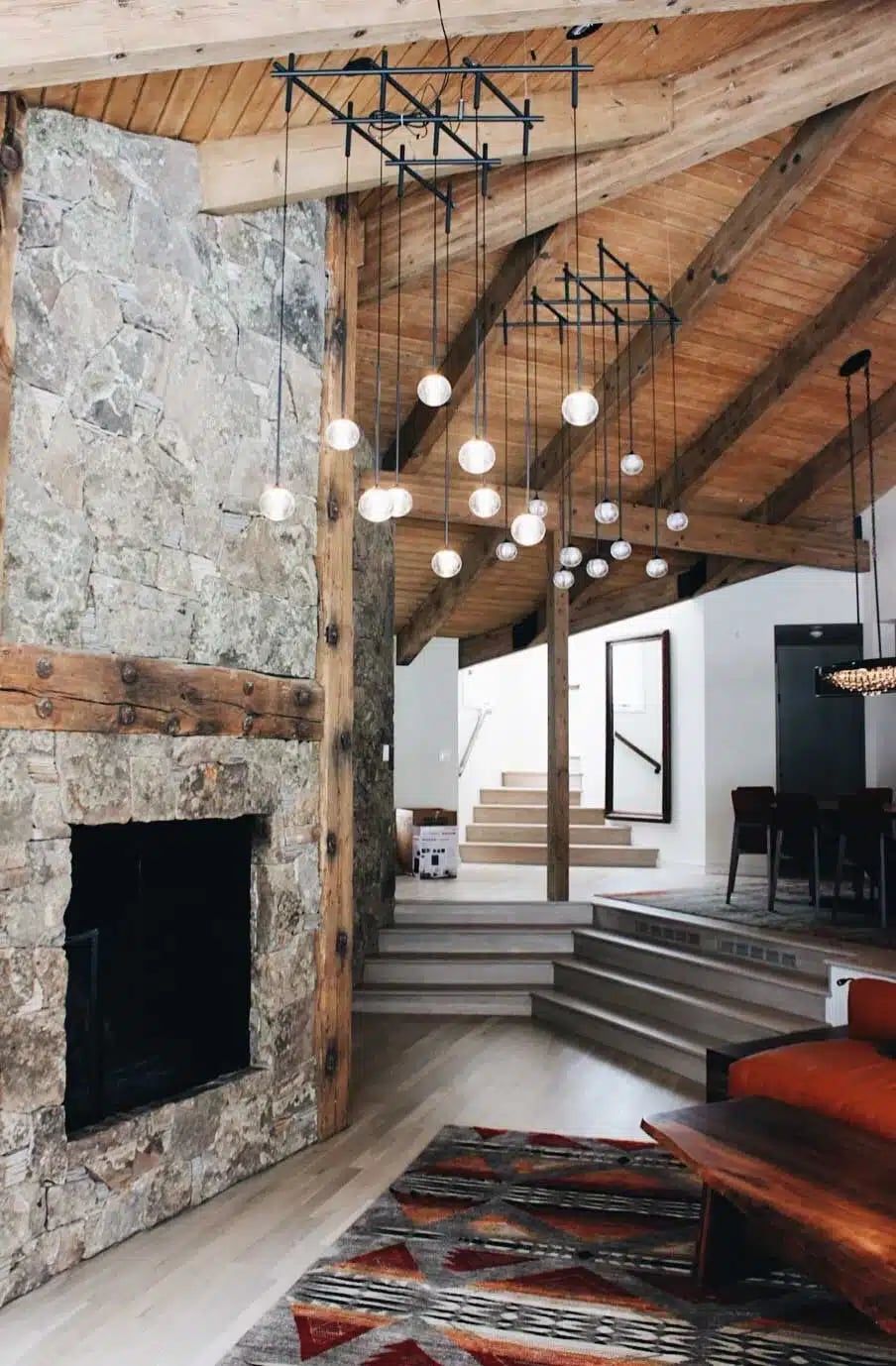 Great room with a floor-to-ceiling stone fireplace, timber beams, wood ceiling and clusters of globe pendant lights
