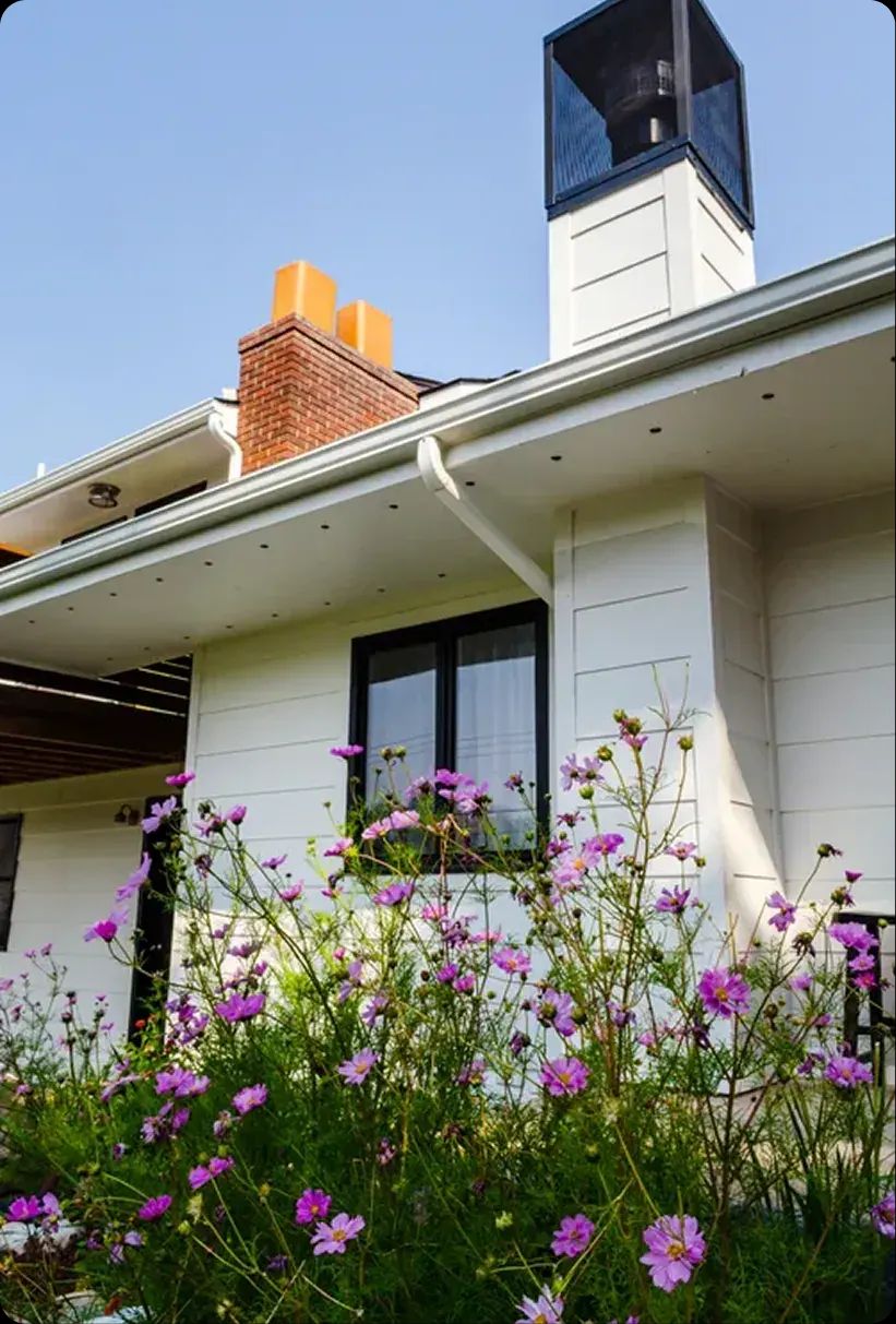 White home exterior with a brick chimney and purple wildflowers