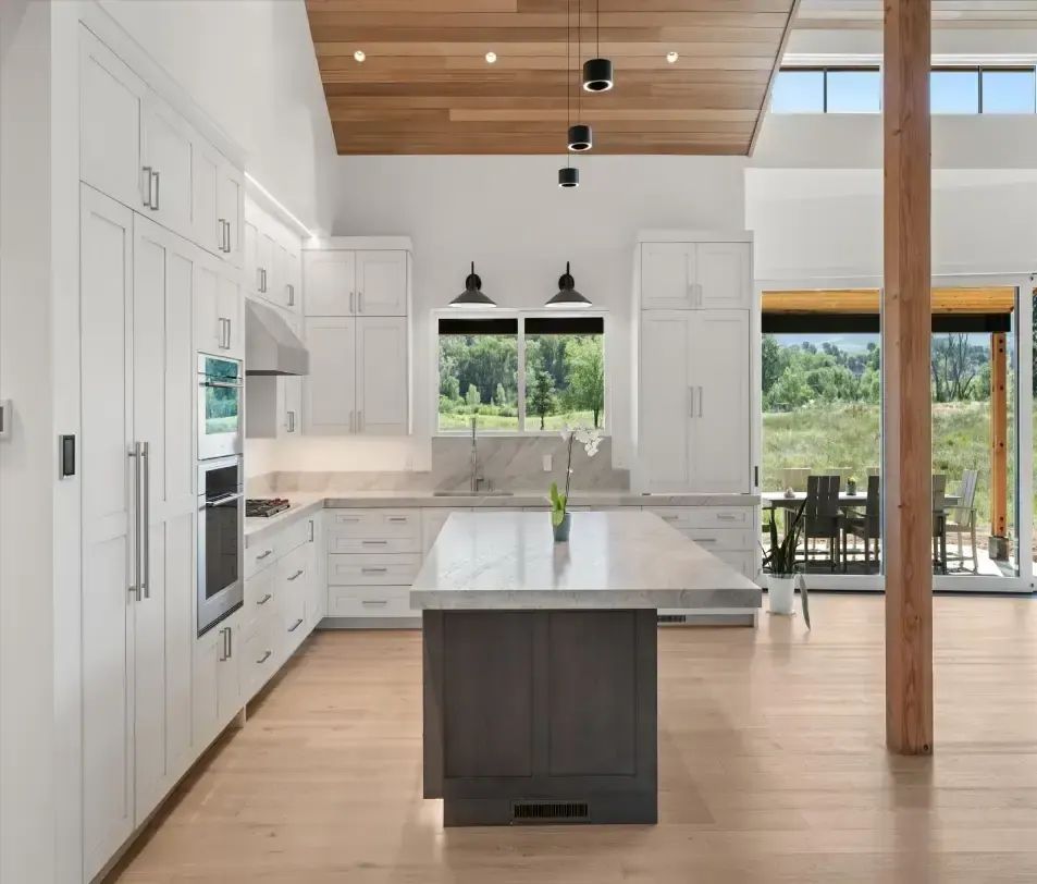 White kitchen with a large island, black pendant lights and a wood ceiling